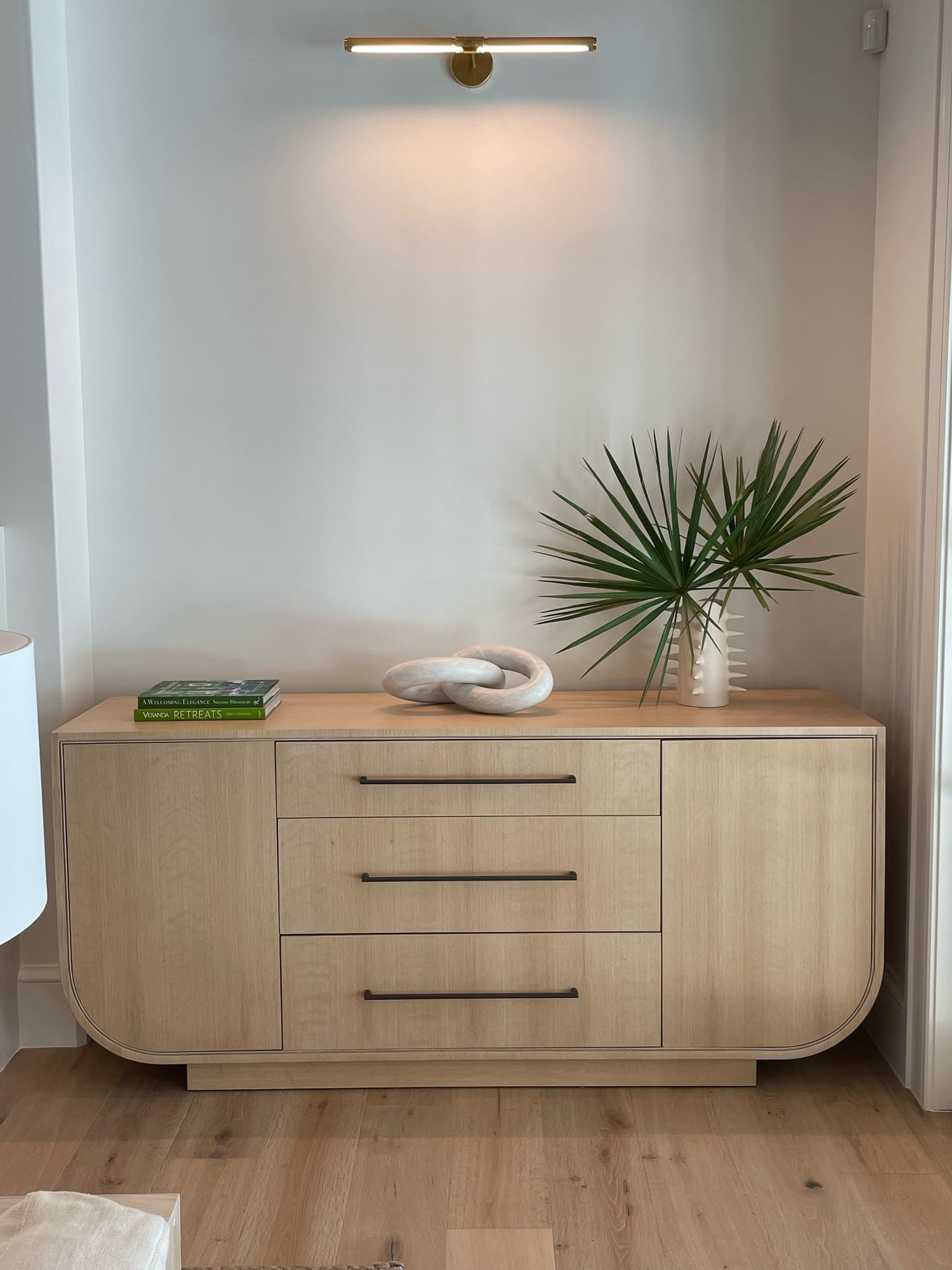 A handcrafted light wood credenza with curved edges, featuring sleek black handles and modern storage.