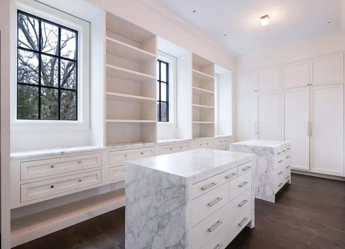 Elegant custom walk-in closet featuring marble islands, built-in shelving, and black-framed windows for natural light.
