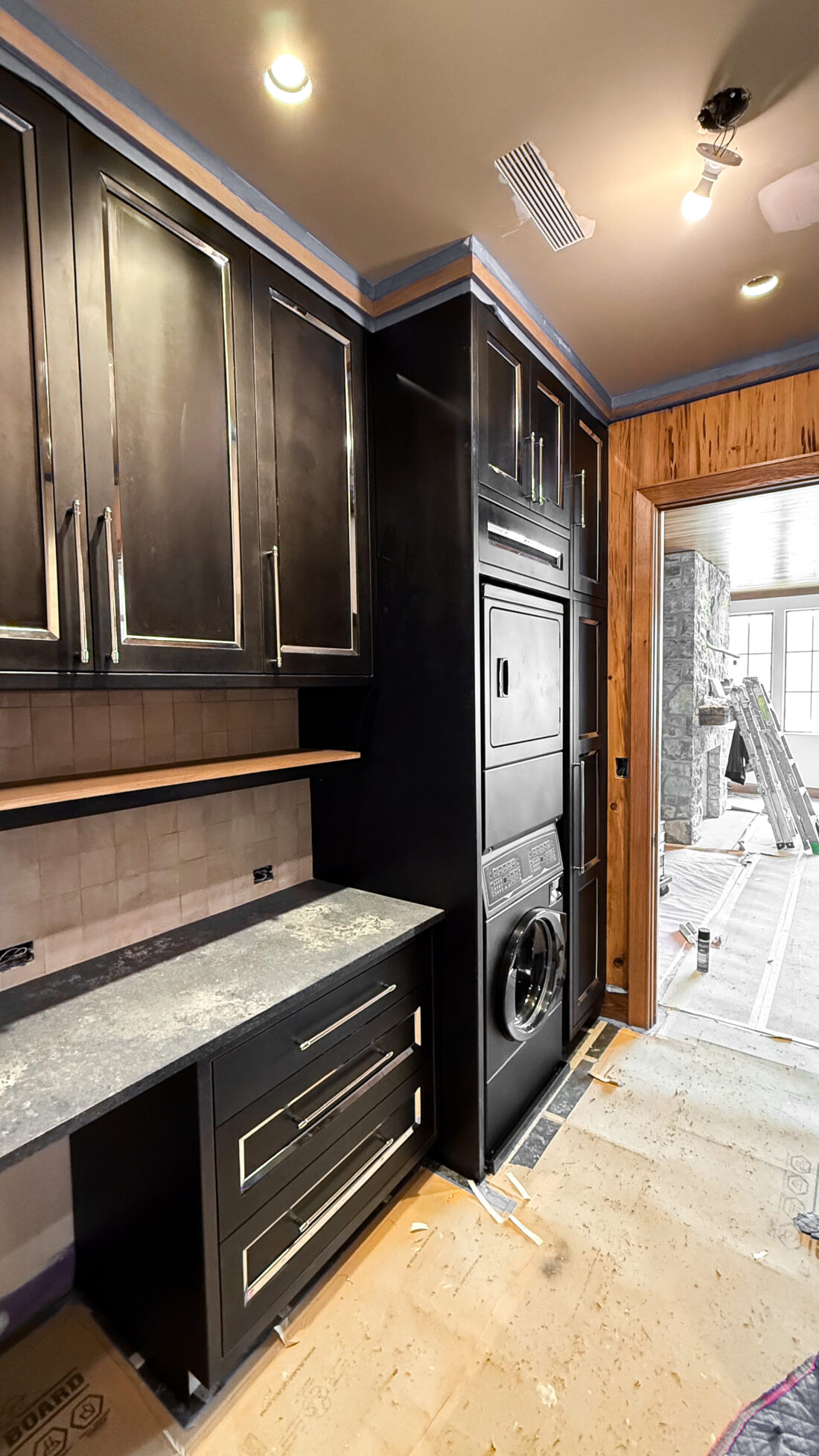 Custom black laundry room cabinets with metallic hardware and stacked washer dryer