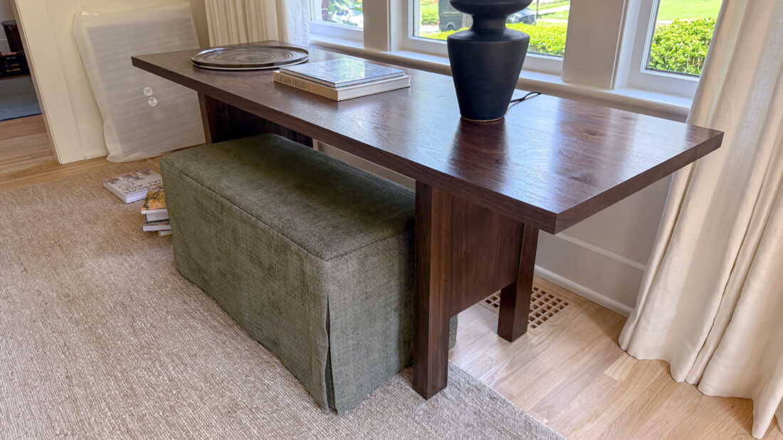 A sleek, custom walnut console table with a minimalist silhouette and bold rectangular supports. Paired with a tailored bench in textured green upholstery, this set offers both style and function — perfect for an entryway, living room, or behind a sofa.