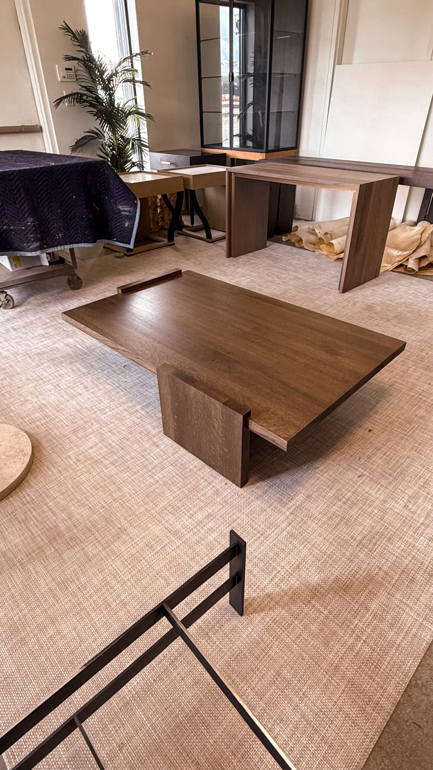Custom oak coffee table with geometric base and a wide rectangular top, highlighting the natural grain of the wood in a modern design studio setting.