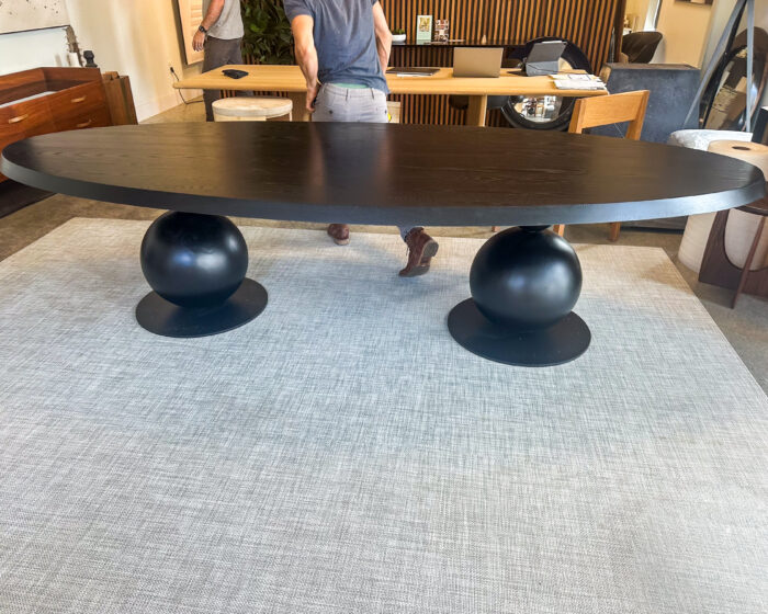 A bold and modern dining table featuring a sleek black oval top supported by sculptural steel sphere bases. Designed to make an unforgettable statement.
