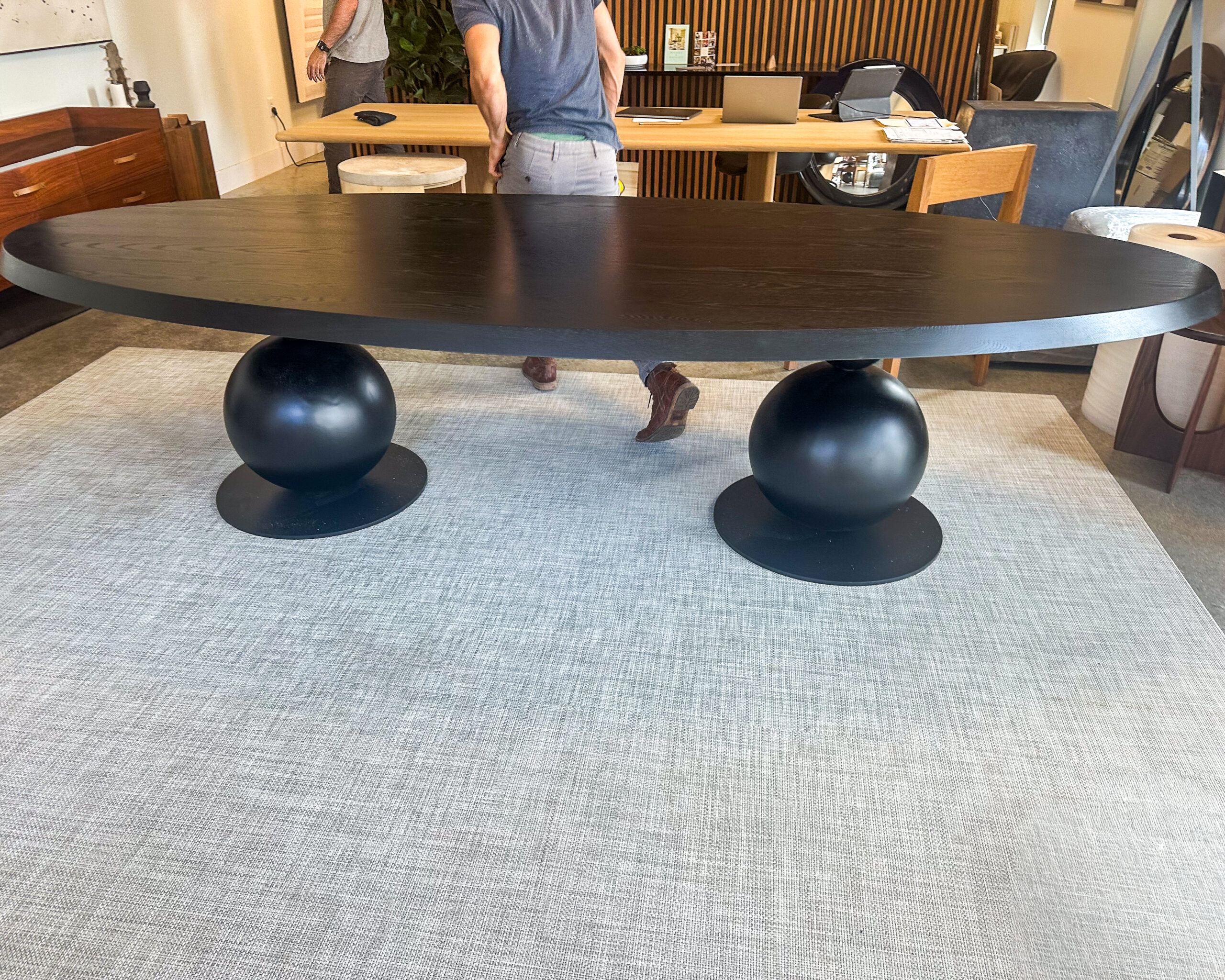 A bold and modern dining table featuring a sleek black oval top supported by sculptural steel sphere bases. Designed to make an unforgettable statement.