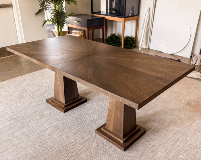 A timeless dining table design featuring a rich wood veneer top and strong plinth-style pedestal bases. Balanced proportions and clean geometry create a refined centerpiece for any dining space.