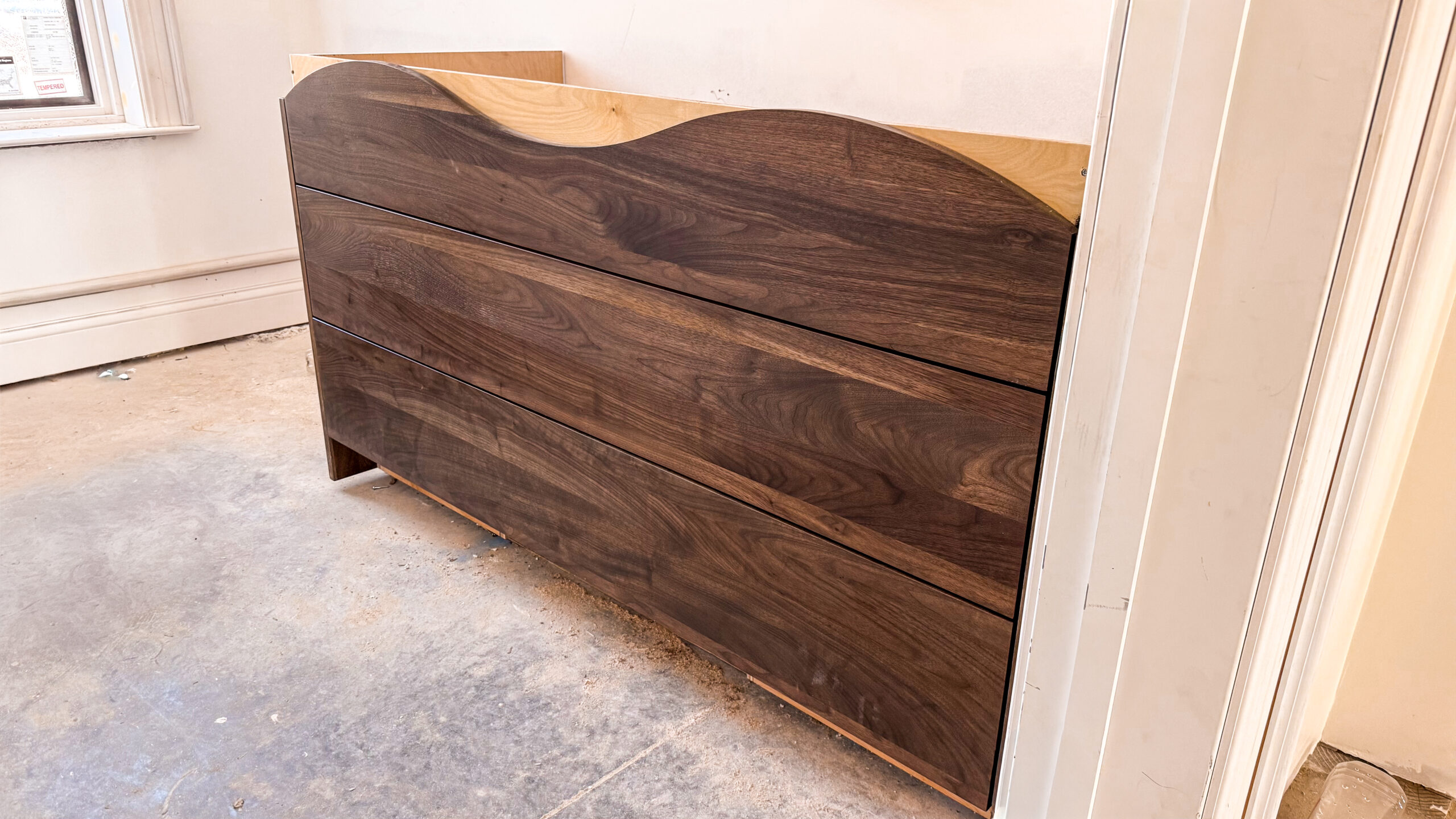 “Custom walnut vanity with flowing wave-shaped top edge and seamless grain cabinetry.”