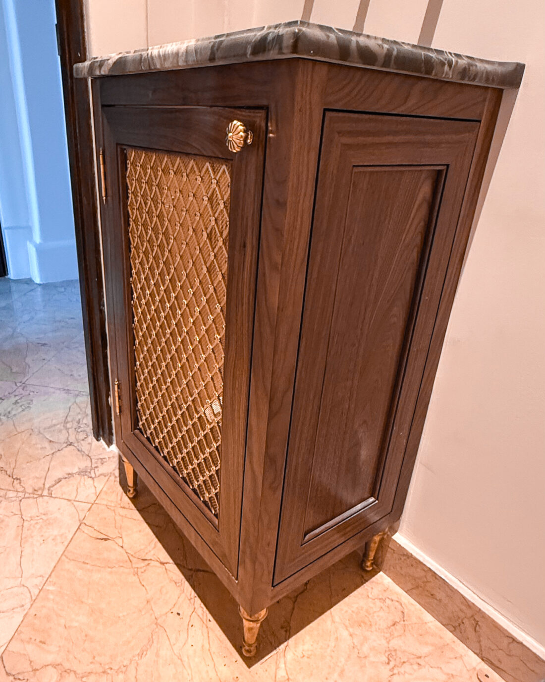 “Custom walnut cabinet with brass grille door, carved marble top, and brass feet.”