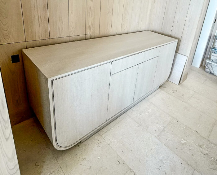Custom white oak credenza with rounded edges and push-to-open doors built into a paneled wall.