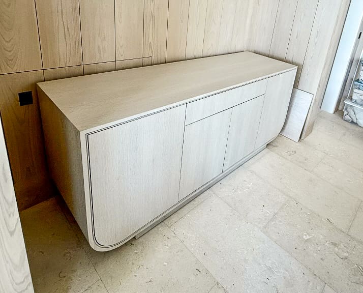 Custom white oak credenza with rounded edges and push-to-open doors built into a paneled wall.